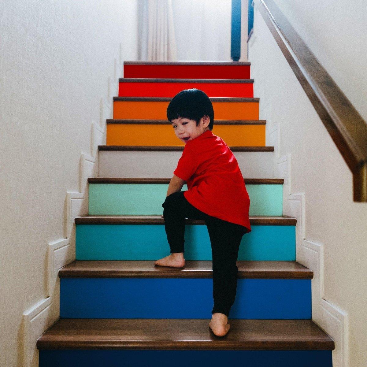 Child playing on a vibrant, multicolored staircase adorned with gradient riser stickers, enhancing home decor.