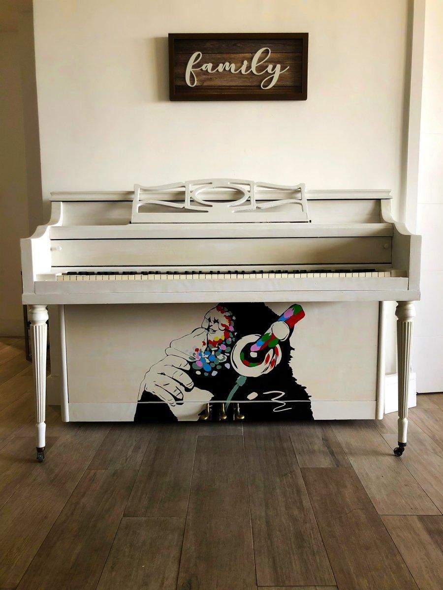 Decorative white piano featuring a colorful monkey design holding headphones in a cozy room setting.