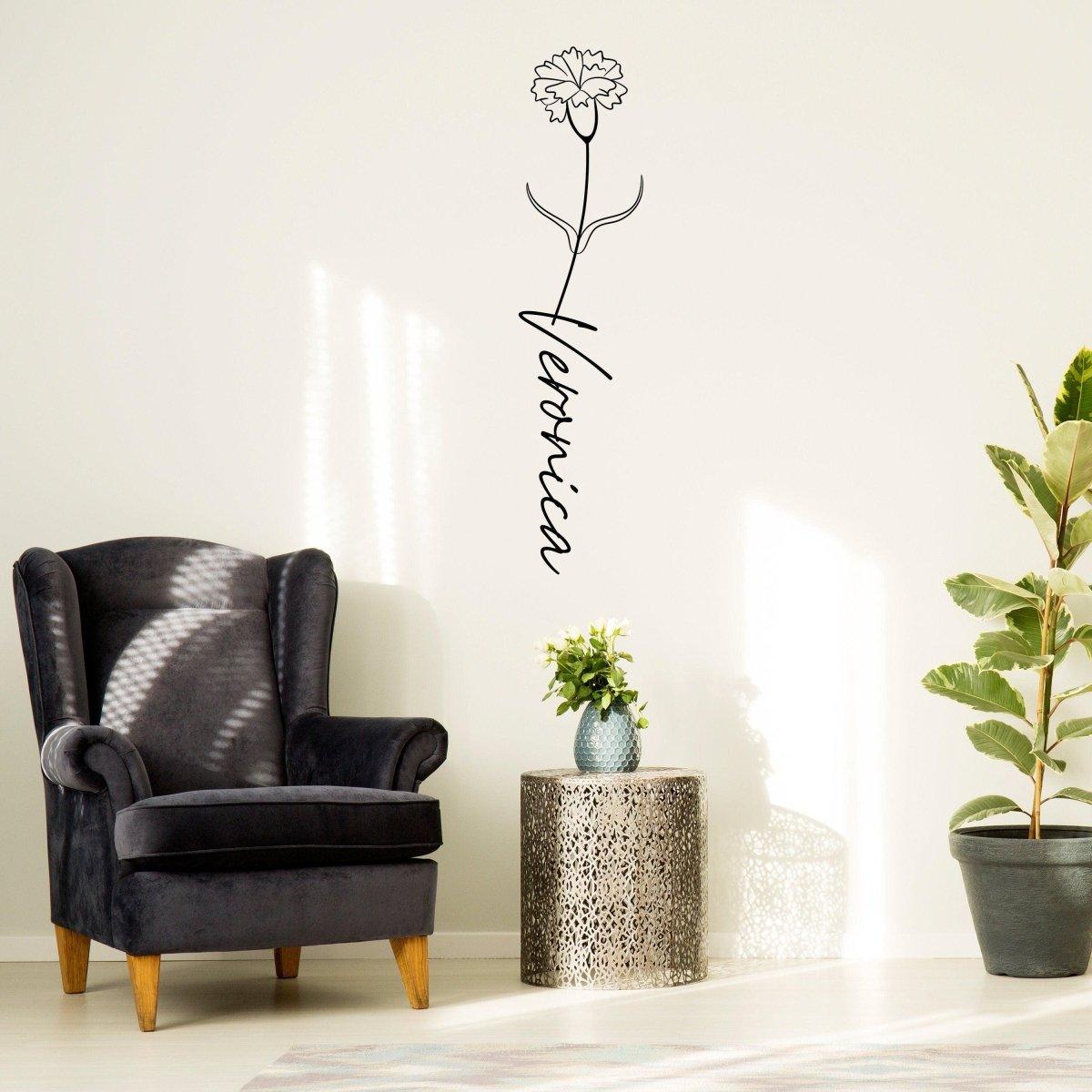 Personalized flower name decal with carnation design on a wall next to a chic armchair and plant.