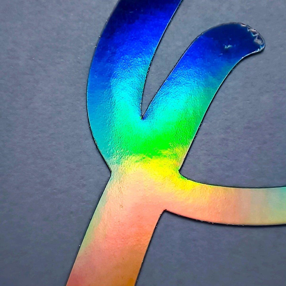 Close-up of a colorful rainbow holographic vinyl decal with shiny surface details on a gray background.