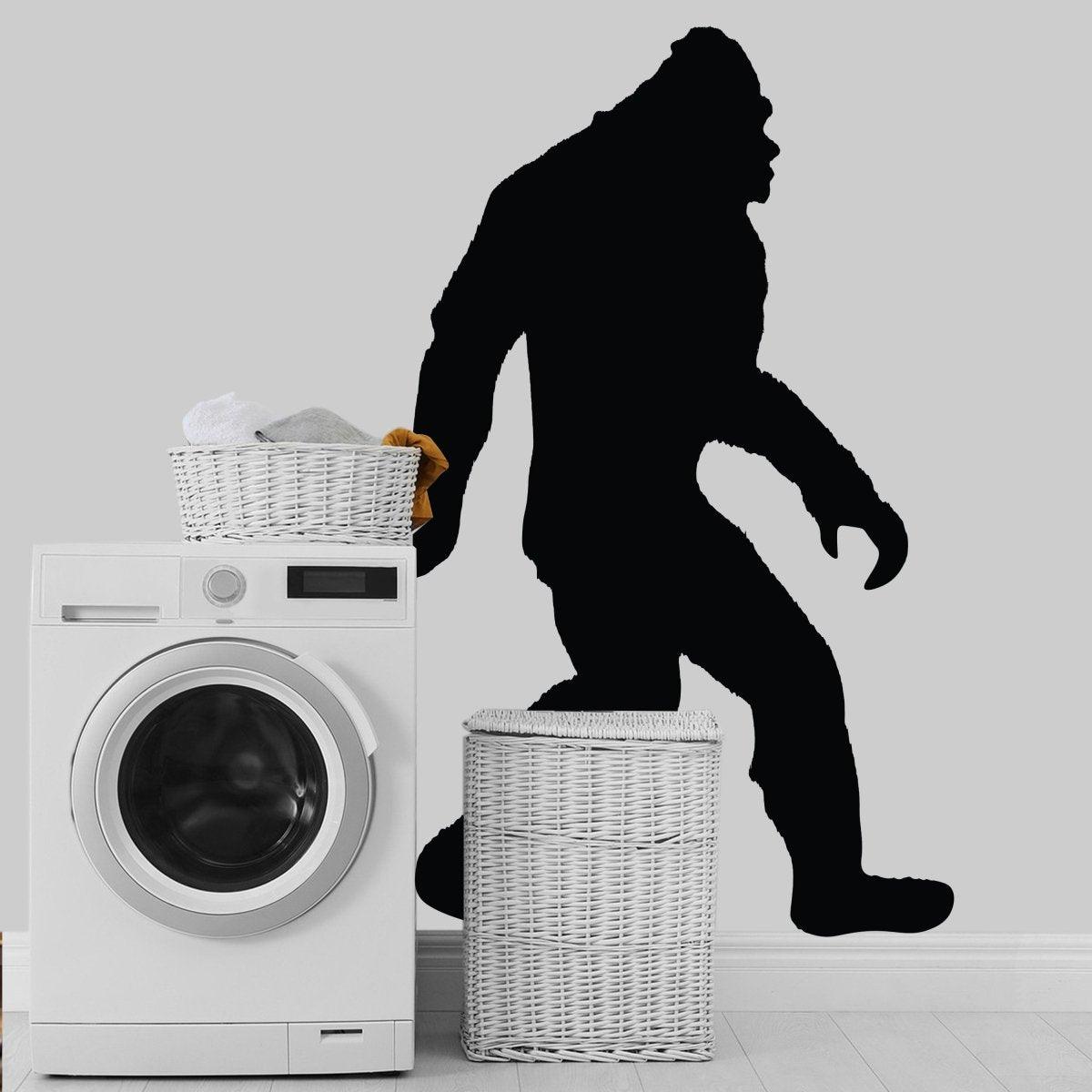 BigFoot vinyl decal silhouette on a wall beside a washing machine and laundry baskets, adding charm to any space.