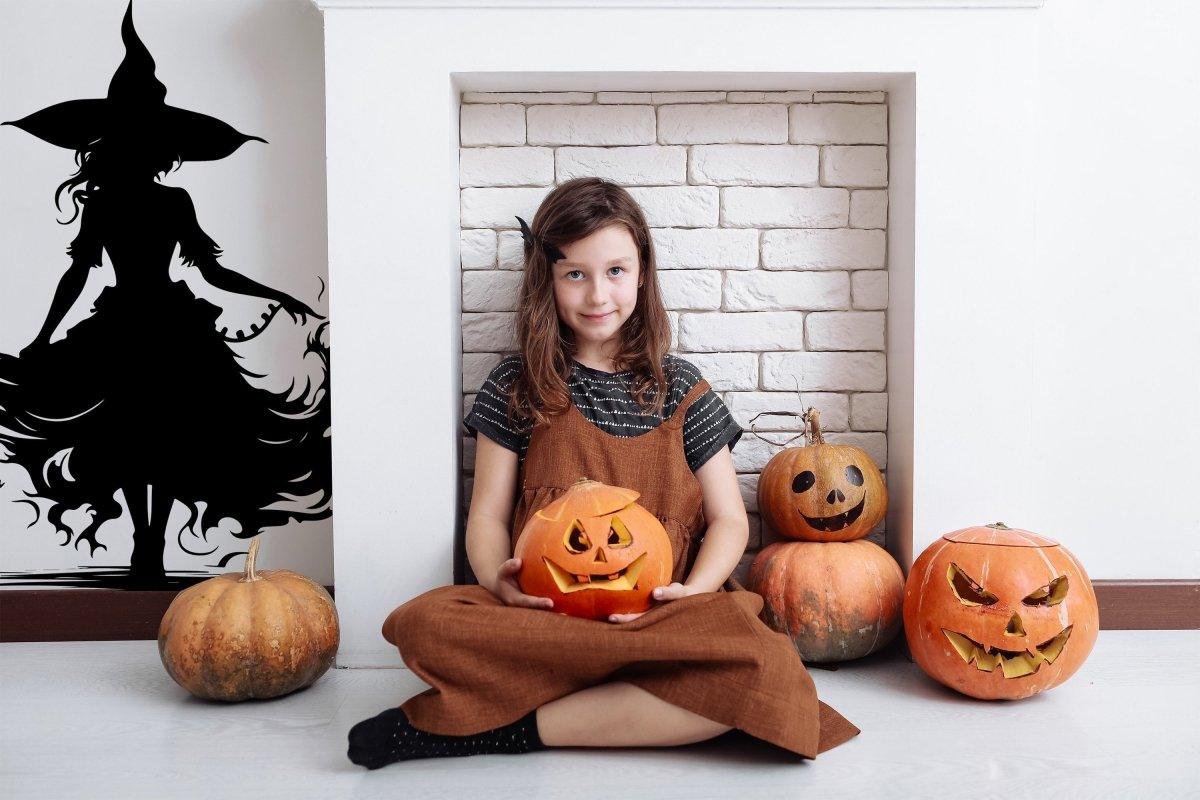 Girl sitting with carved pumpkins, mystical witch silhouette decor on the wall for enchanting Halloween atmosphere.