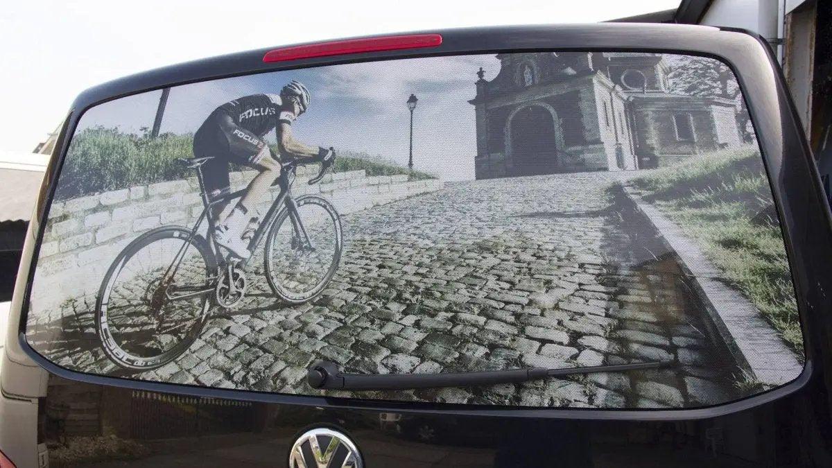 Rear window graphic of a cyclist on a cobblestone path, showcasing a custom vision protection film design.