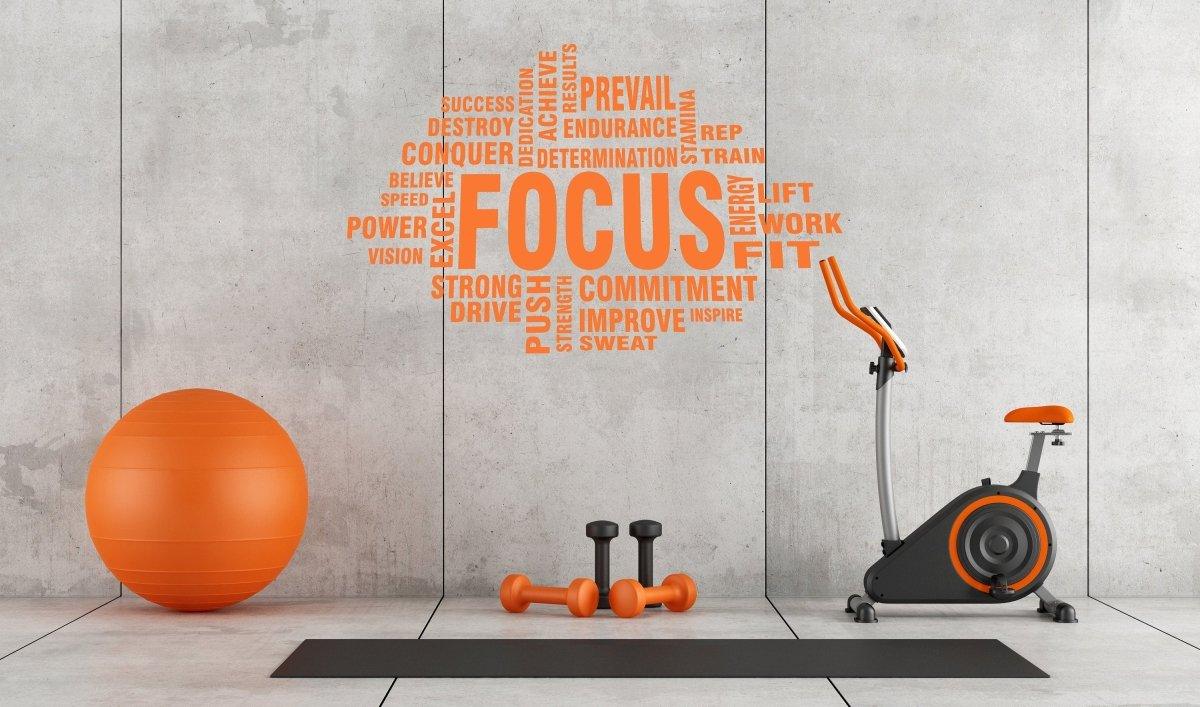 Inspirational fitness wall sticker with the word 'FOCUS' amidst motivational words, set in a modern home gym.