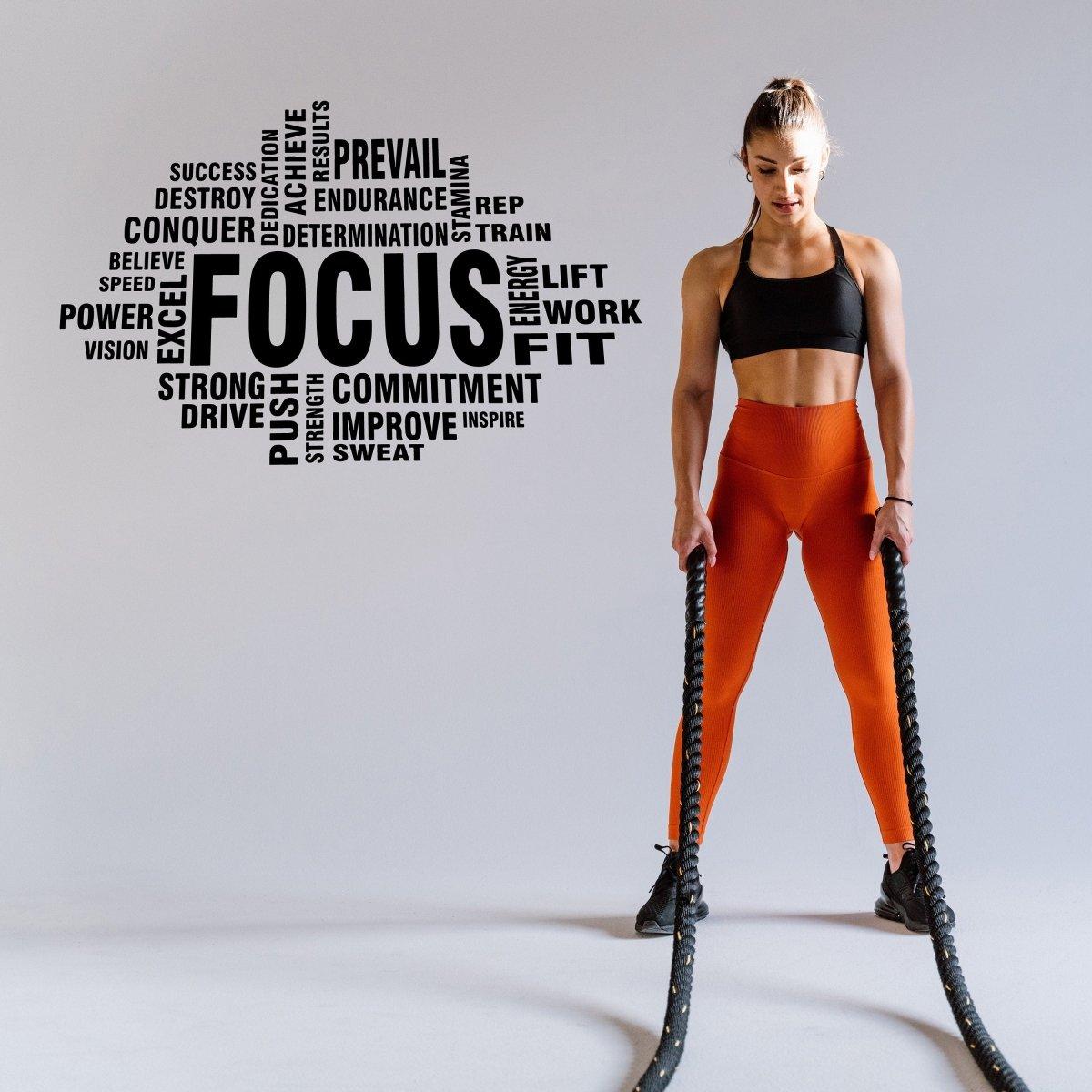 Woman exercising with battle ropes and motivational fitness words on the wall, inspiring focus and commitment.