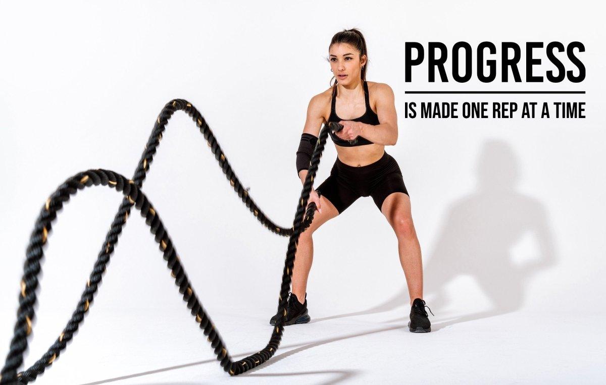 Woman exercising with battle ropes, displaying fitness motivation quote 'Progress is made one rep at a time'