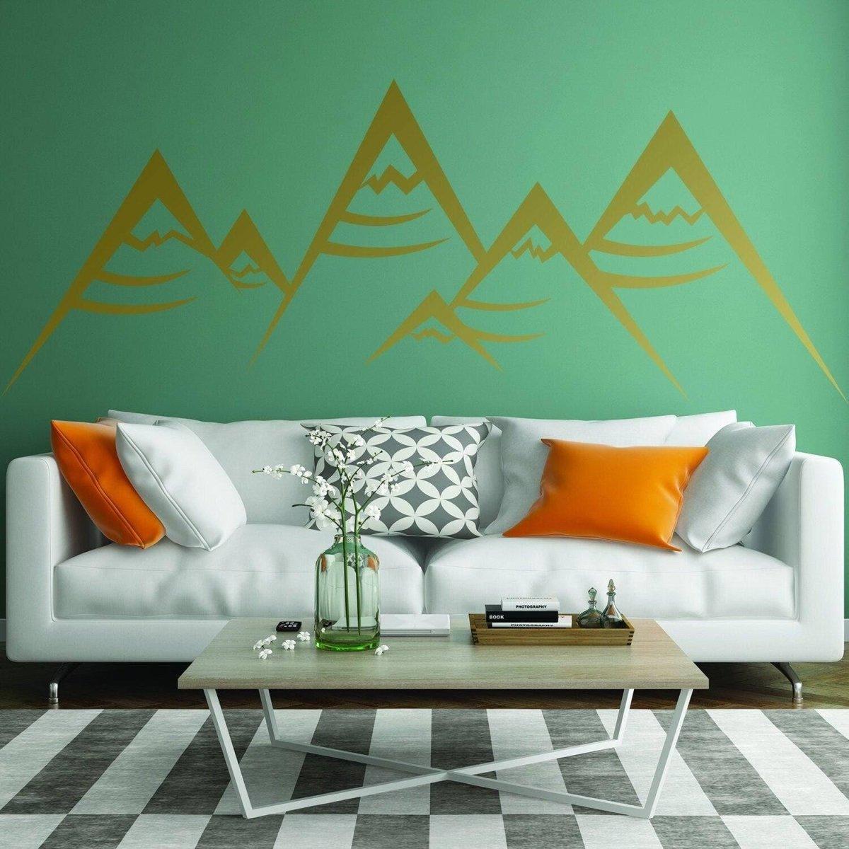 Boho modern vinyl wall decal of geometric peaks in gold on green wall above stylish sofa with colorful cushions.
