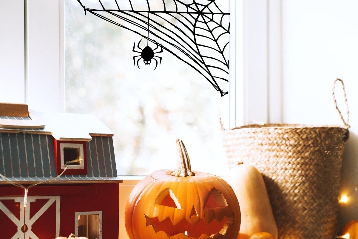 Halloween spider web wall decal with a spider, adding spooky decor to a window, pumpkin and decorations in the foreground.