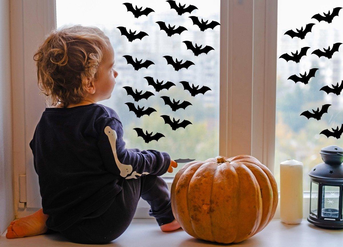 Child admiring Halloween bat window stickers with a pumpkin and lantern, creating a spooky atmosphere.