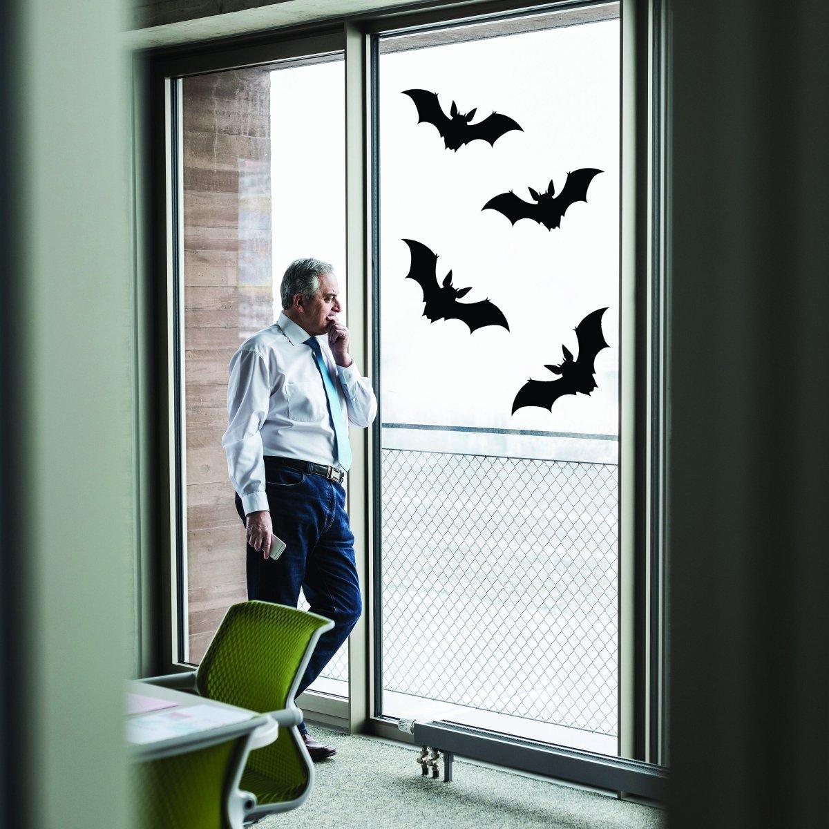 Man standing by a window with Halloween bat stickers, showcasing spooky seasonal decor.