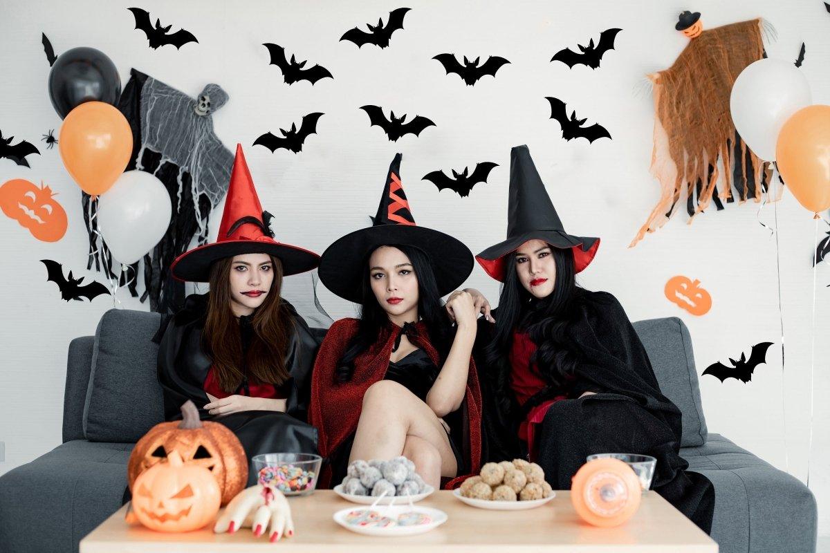 Three women in Halloween costumes with witch hats, surrounded by Halloween decorations and treats.