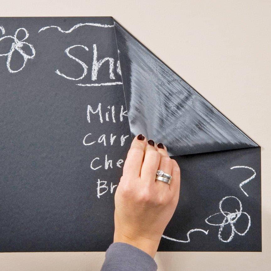 Hand peeling a chalkboard wall sticker with grocery list written in chalk on a smooth surface.