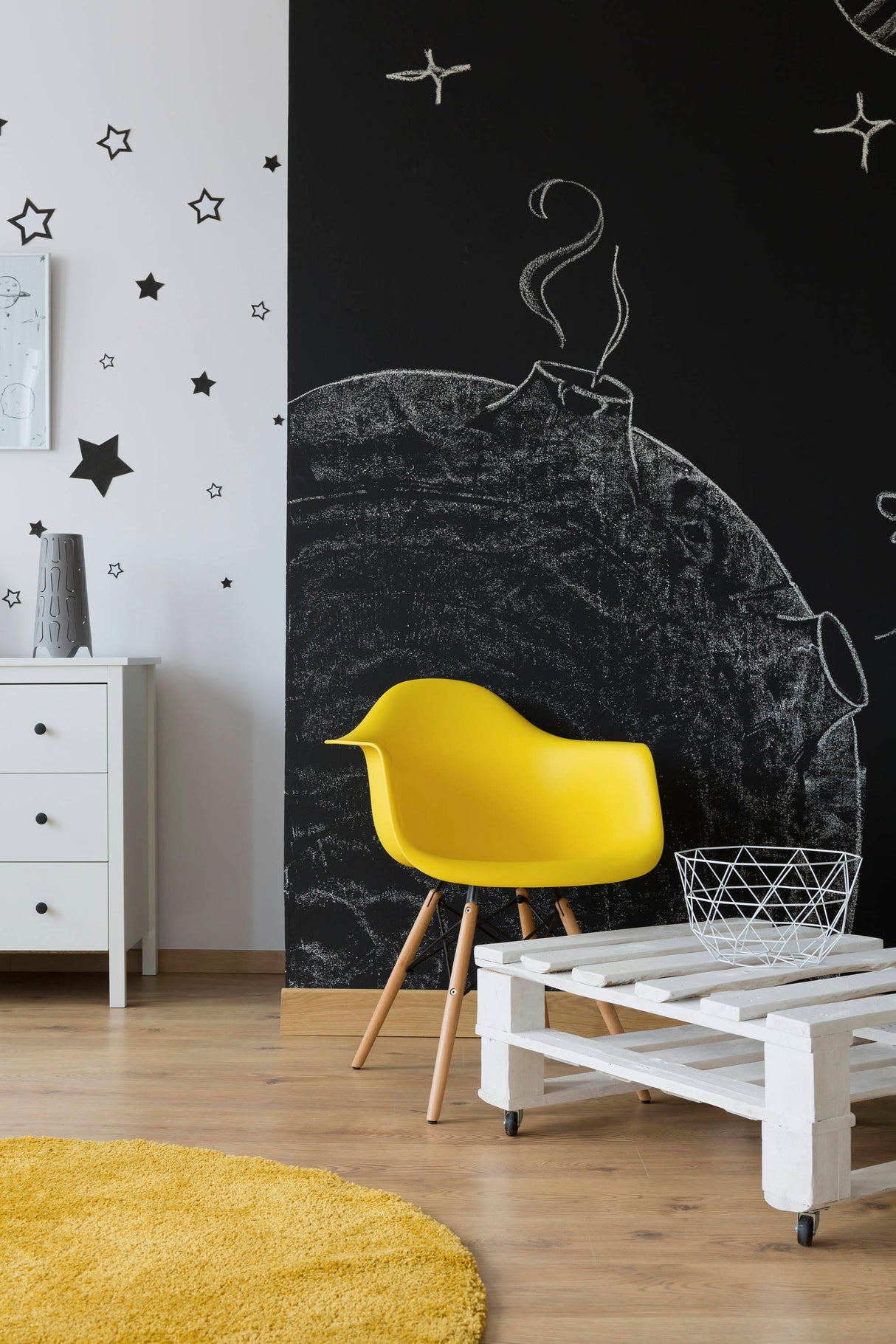 Stylish room featuring a black chalkboard wall with stars, a bright yellow chair, and a white wooden table.