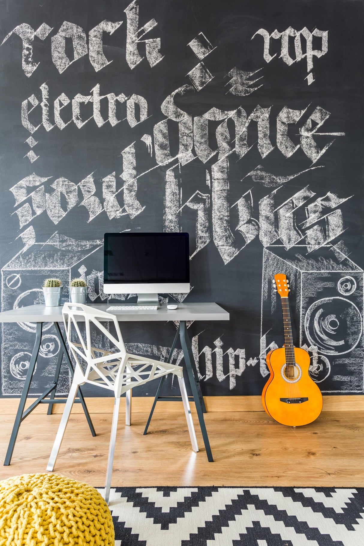 Stylish home office with a chalkboard wall art featuring music genres and a desk with a computer and guitar.