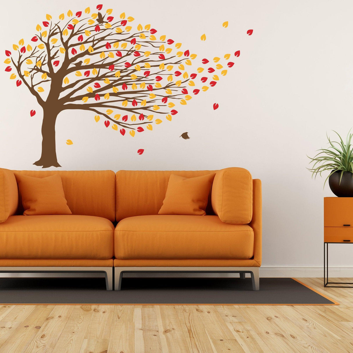 Large autumn tree wall decal with colorful leaves above an orange couch in a cozy living room.