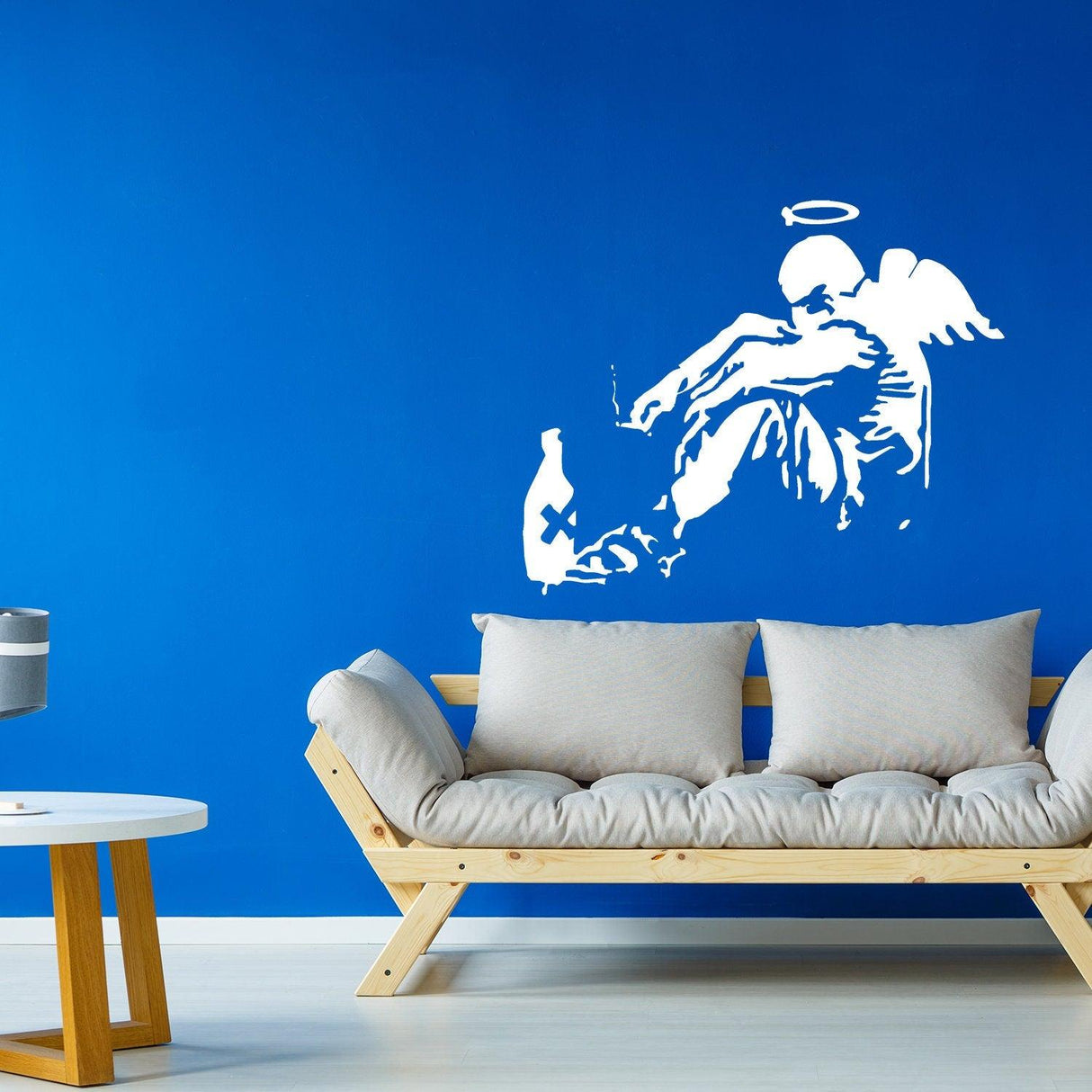 Banksy Fallen Angel wall sticker on blue wall, featuring angel sitting with wings and halo, stylish urban art decor.