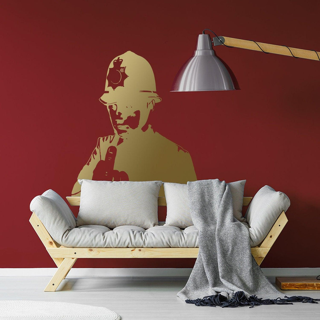 Banksy-inspired middle finger policeman wall decal in gold on a red wall above a cozy couch.