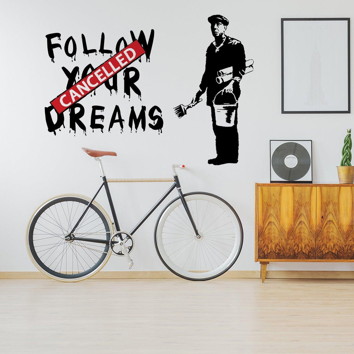 Banksy Follow Your Dreams wall sticker with cancelled message, featuring a homeless figure in a home setting.
