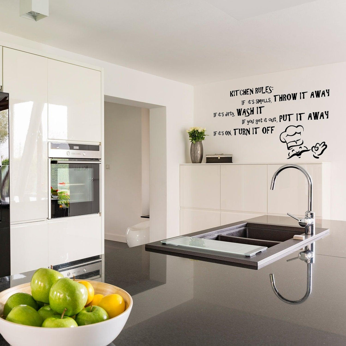 Modern kitchen featuring a humorous kitchen rules wall sticker above a sleek black countertop.