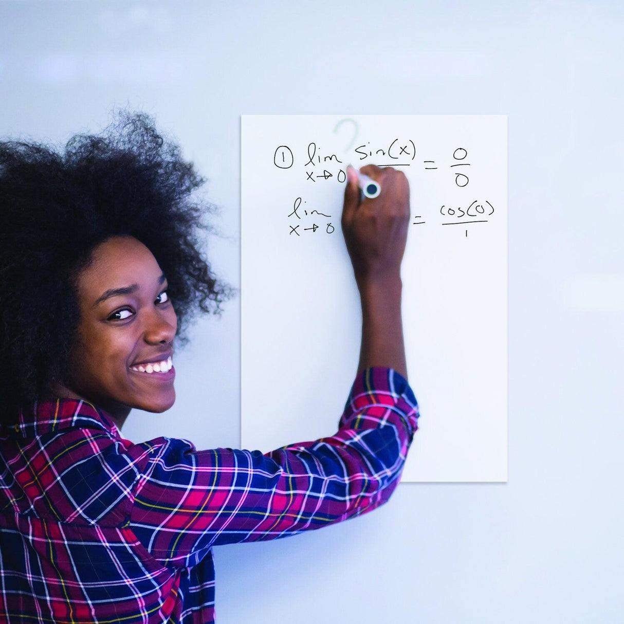 Smiling woman writing math equations on a whiteboard sticker in a classroom setting.