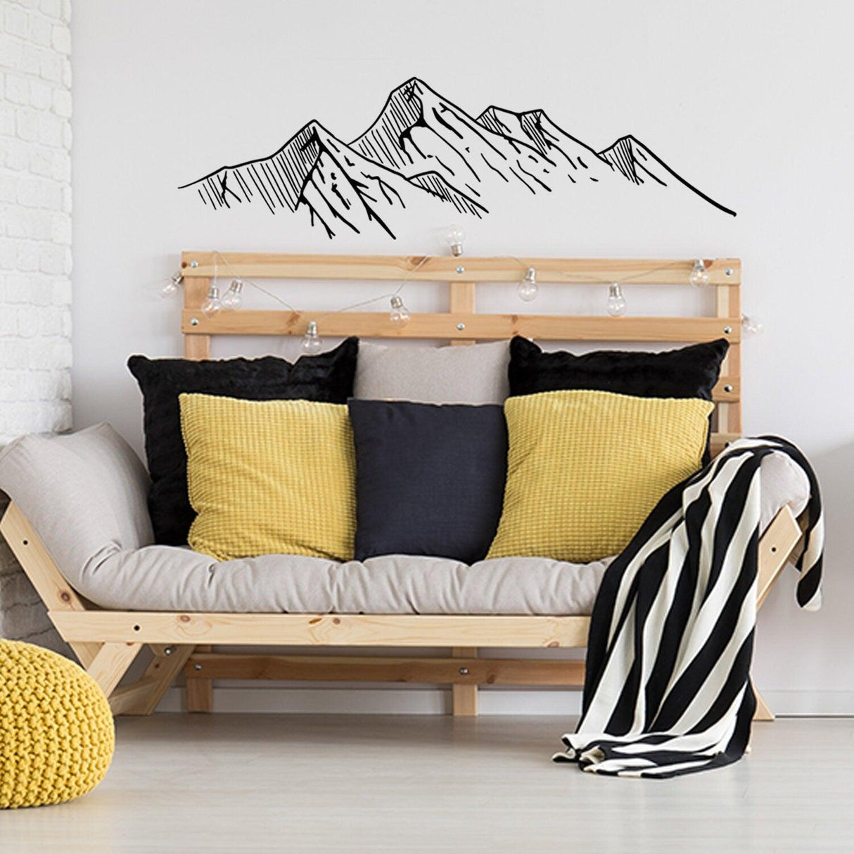 Mountain silhouette wall decal above a cozy sofa with yellow and black pillows in a modern living room.