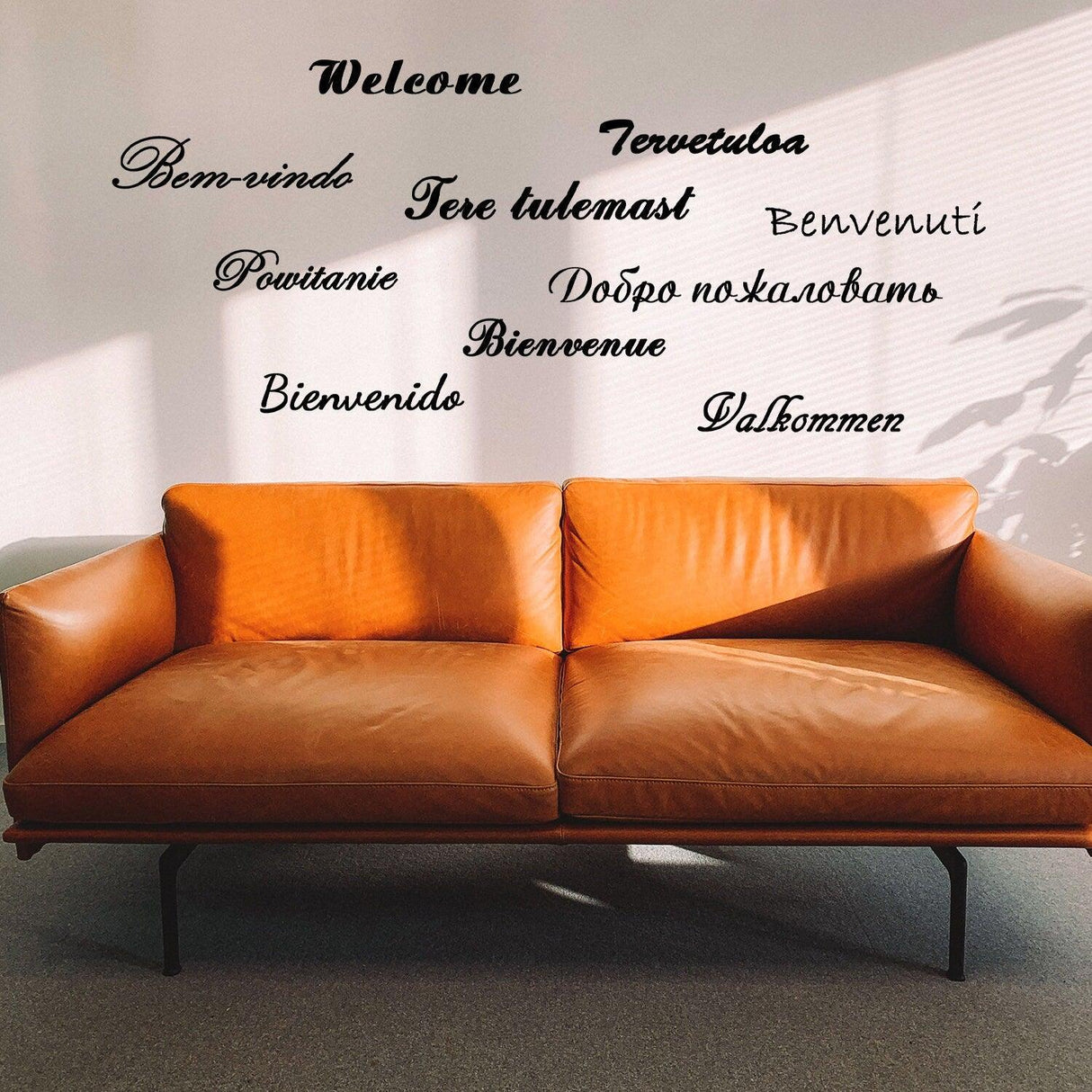 Welcome vinyl wall stickers in various languages above a stylish brown sofa, adding elegance to home decor.
