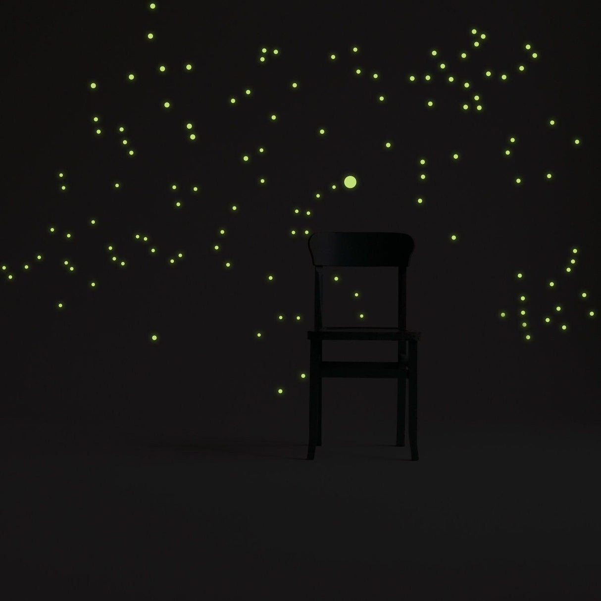 Night glowing star wall stickers creating a luminescent effect around a chair in a dark room.