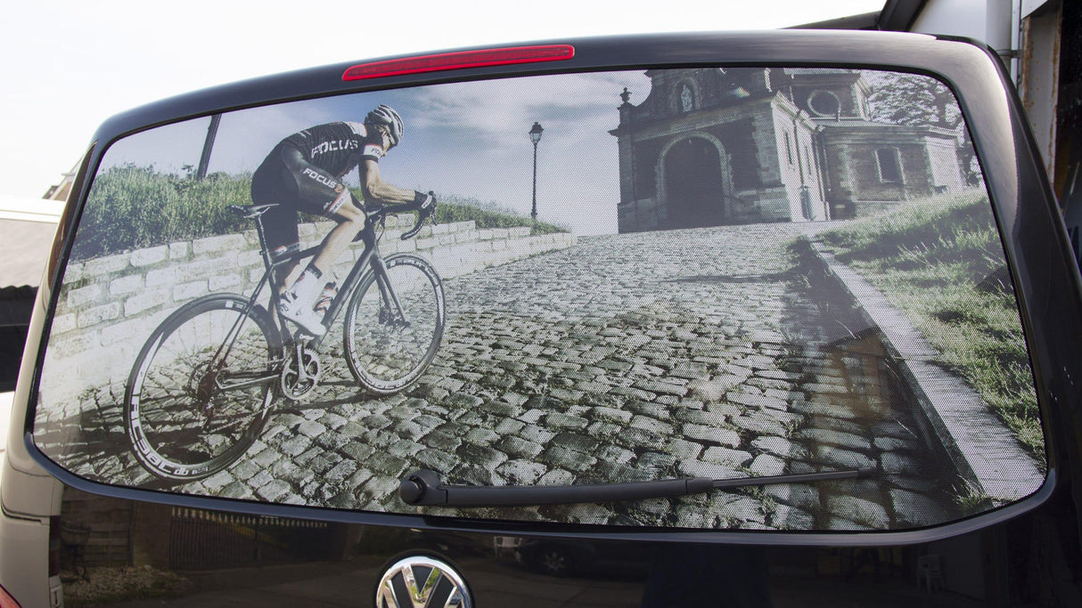 Bicycle rear window decal featuring a cyclist climbing a cobblestone hill near an old building.