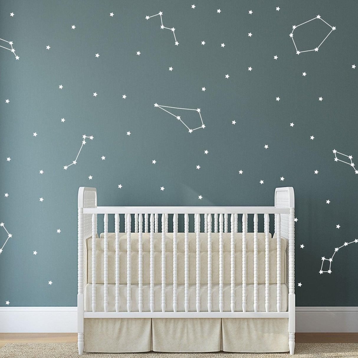 Vinyl wall stickers depicting zodiac constellations on a dark wall above a white crib, creating a celestial nursery decor.