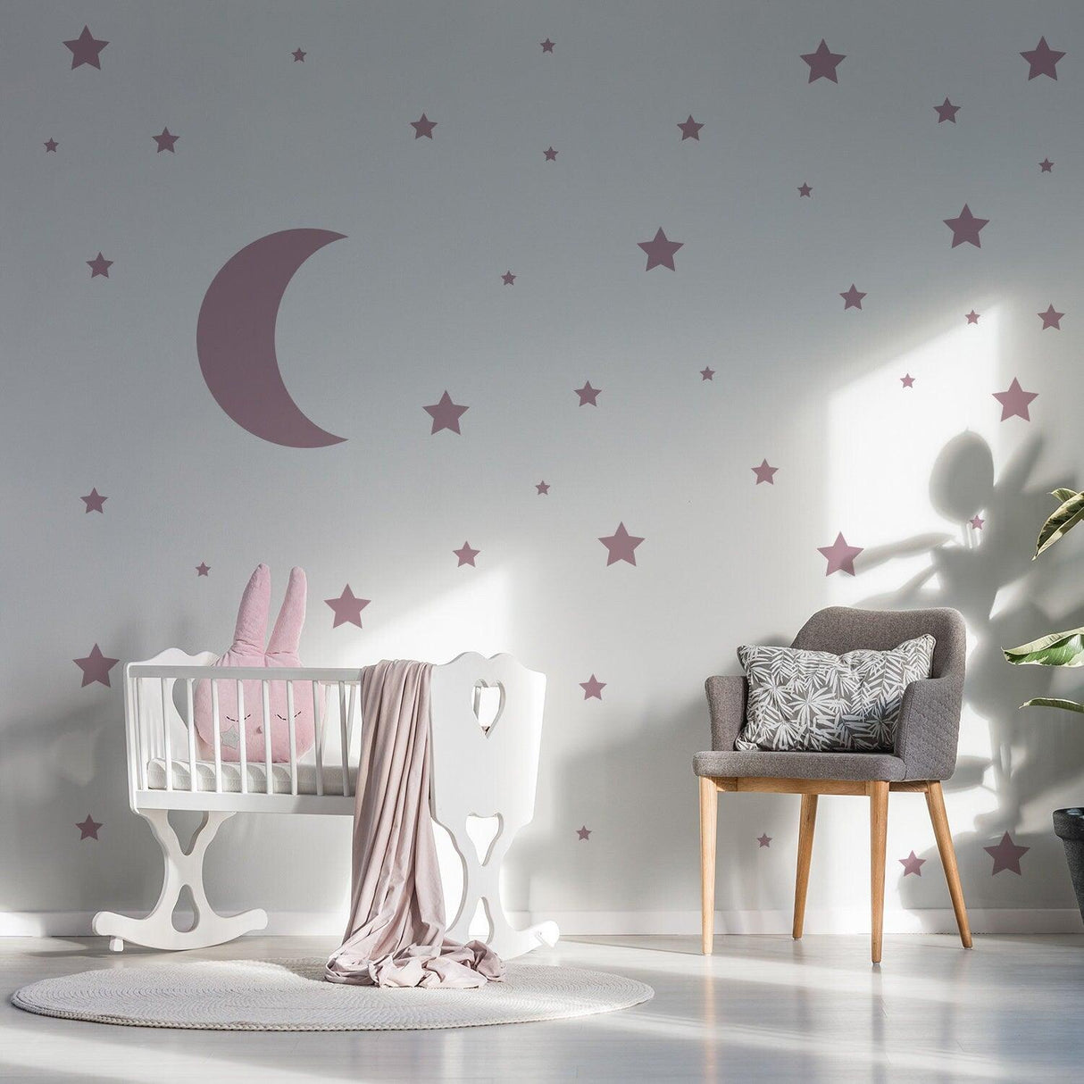 Nursery wall decorated with pink star and moon stickers, featuring a crib and cozy chair.