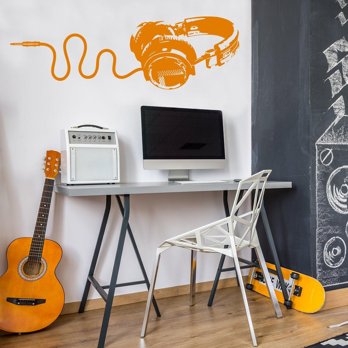 Headphones vinyl wall sticker in orange above a desk with guitar and monitor, adding musical decor to a modern workspace.