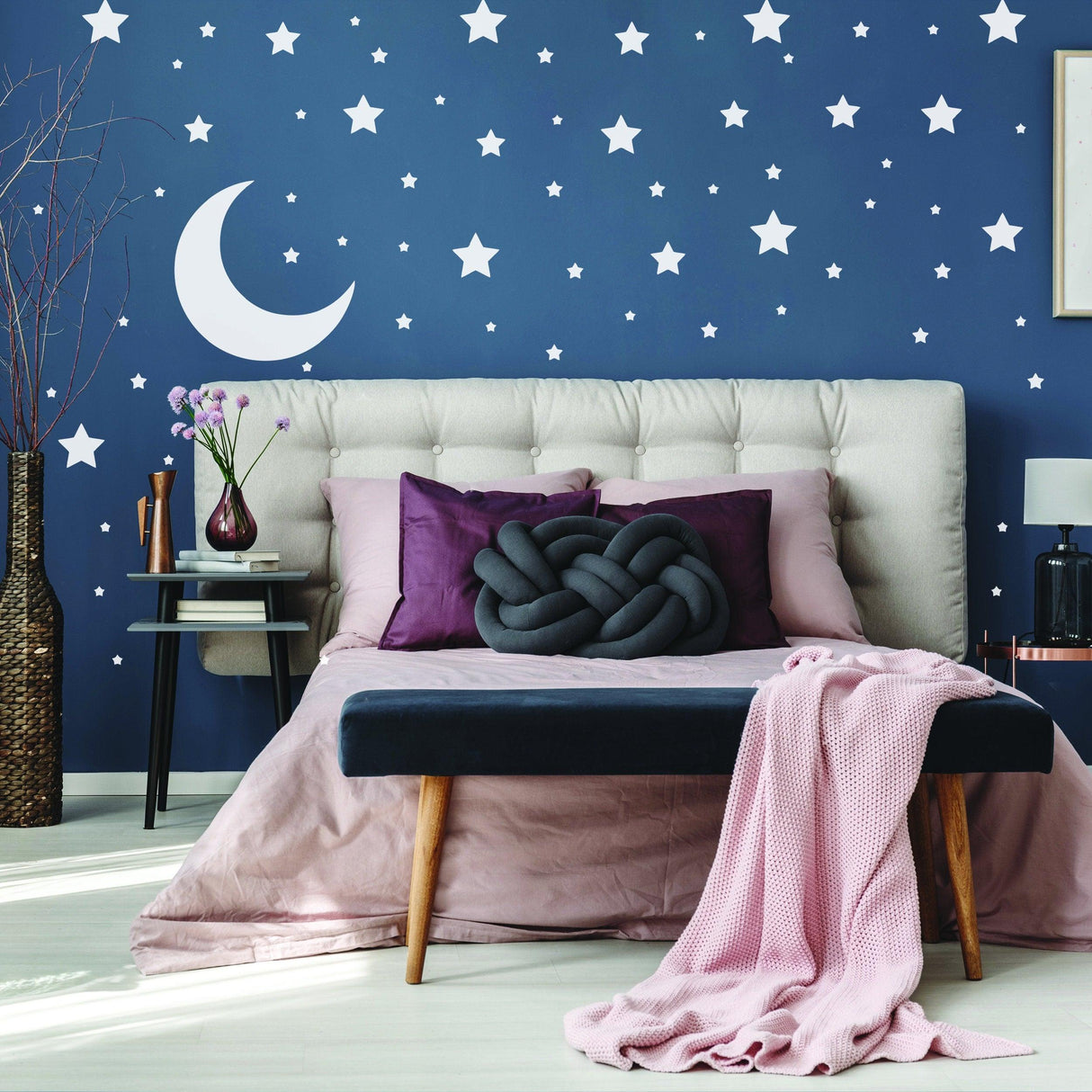 Bedroom with navy blue wall decorated with white stars and a moon, featuring a cozy bed and soft textiles.