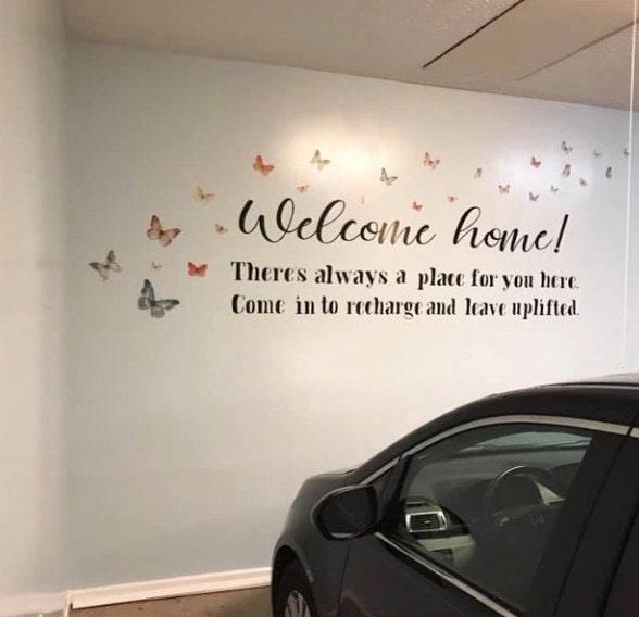 Vinyl wall decal with butterflies and the text 'Welcome home! There's always a place for you here' in a garage.
