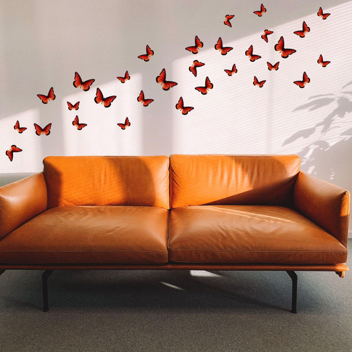 30 butterfly wall decor stickers displayed above a brown leather sofa in a stylish room.