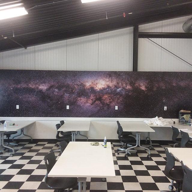Stunning galaxy mural on wall featuring deep space design with stars, set in a classroom with black and white checkered flooring.