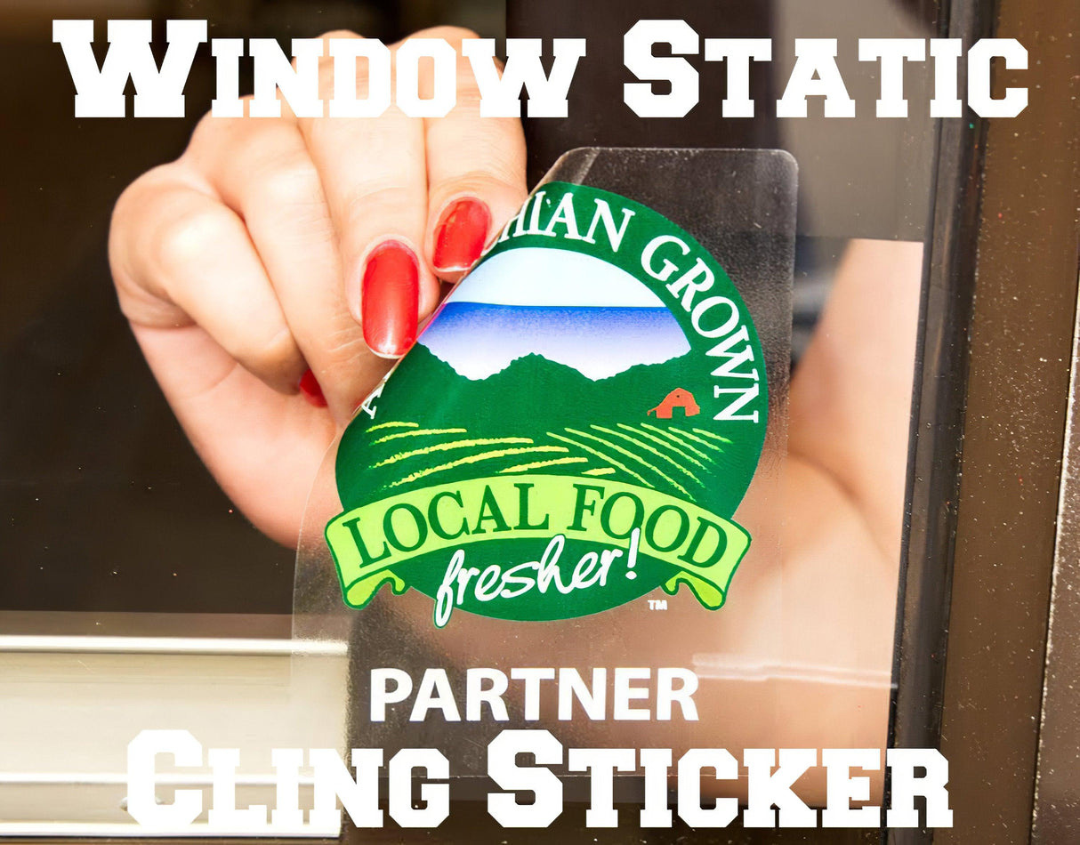 Hand placing a window static cling sticker promoting local food on a glass surface.