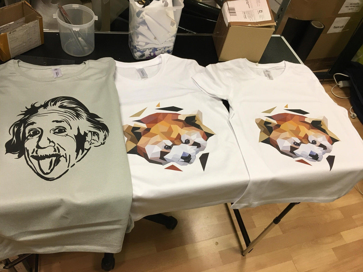 Three custom t-shirts featuring unique designs: an Einstein graphic, a colorful dog illustration, and a geometric pattern.
