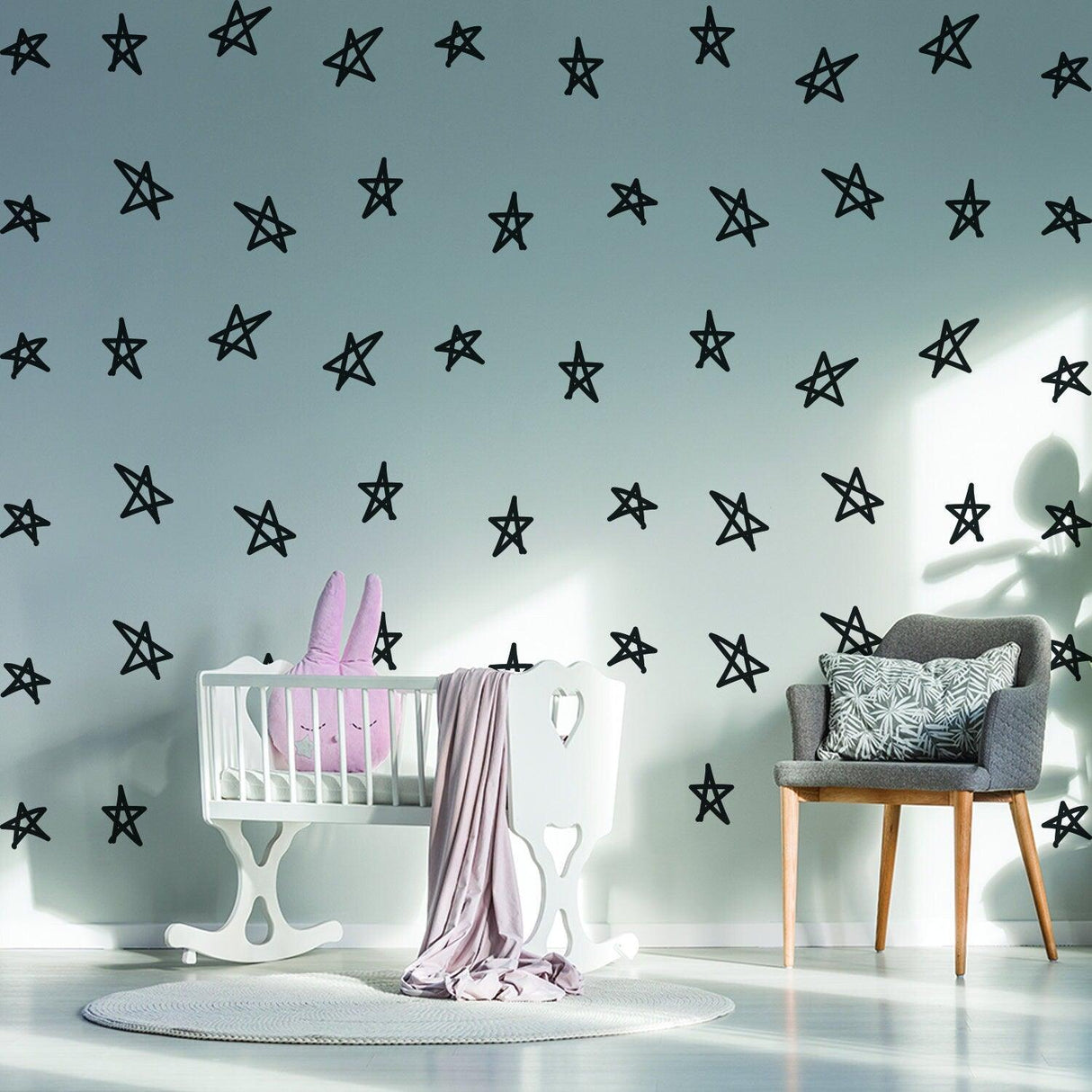 Decorative black star stickers on the wall above a baby crib with a plush bunny and cozy chair in a nursery.