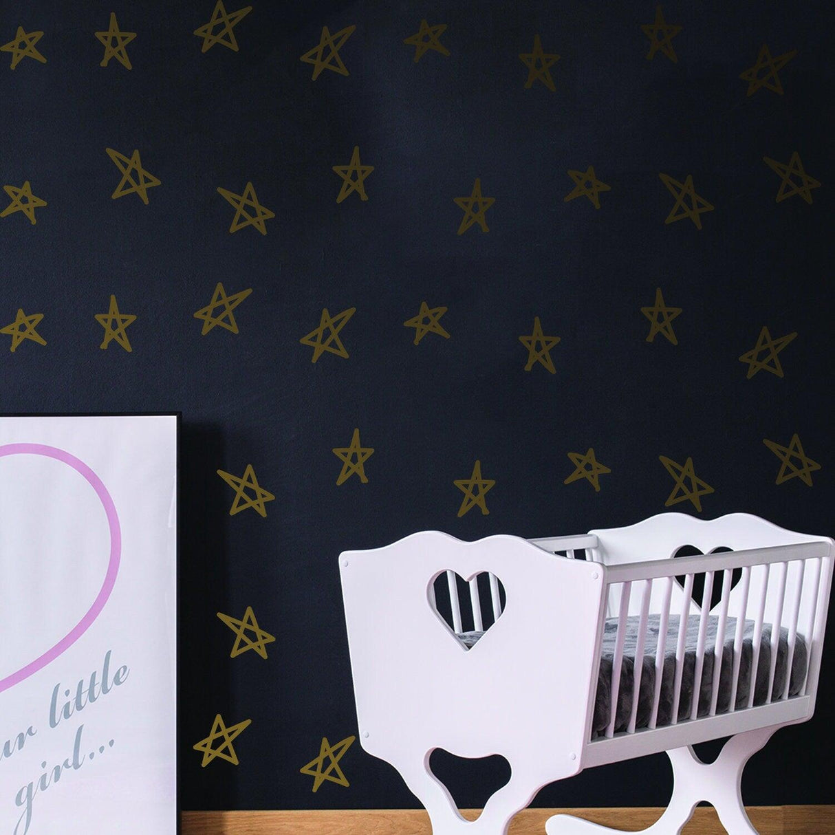 Gold star stickers on a dark wall, with a white crib and artwork for baby shower decor.