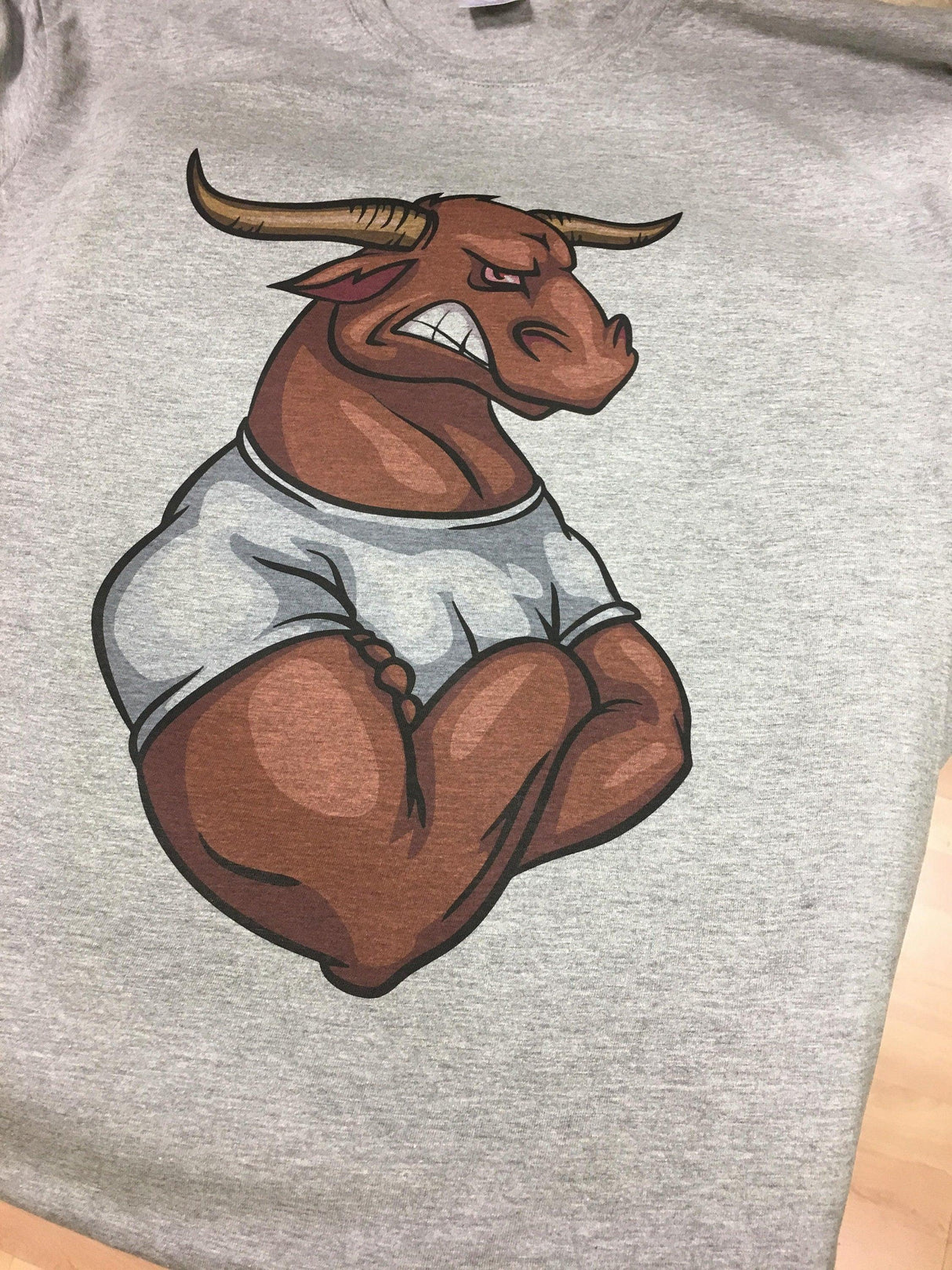 Graphic of a muscular bull character wearing a t-shirt, showcasing a bold design on a gray background.