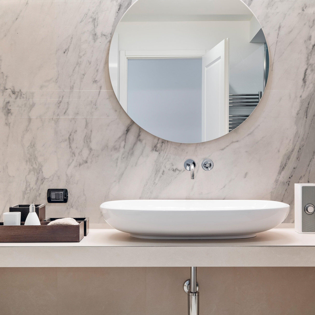 Modern bathroom featuring a circular mirror above a white vessel sink and marble wall, creating a luxurious atmosphere.