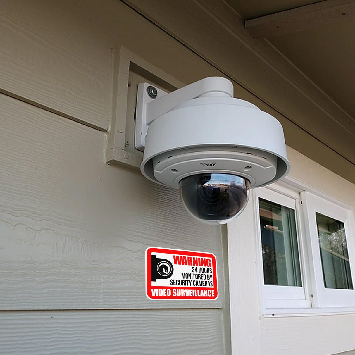 Video camera surveillance mounted outside a building with a security warning sign beneath it.