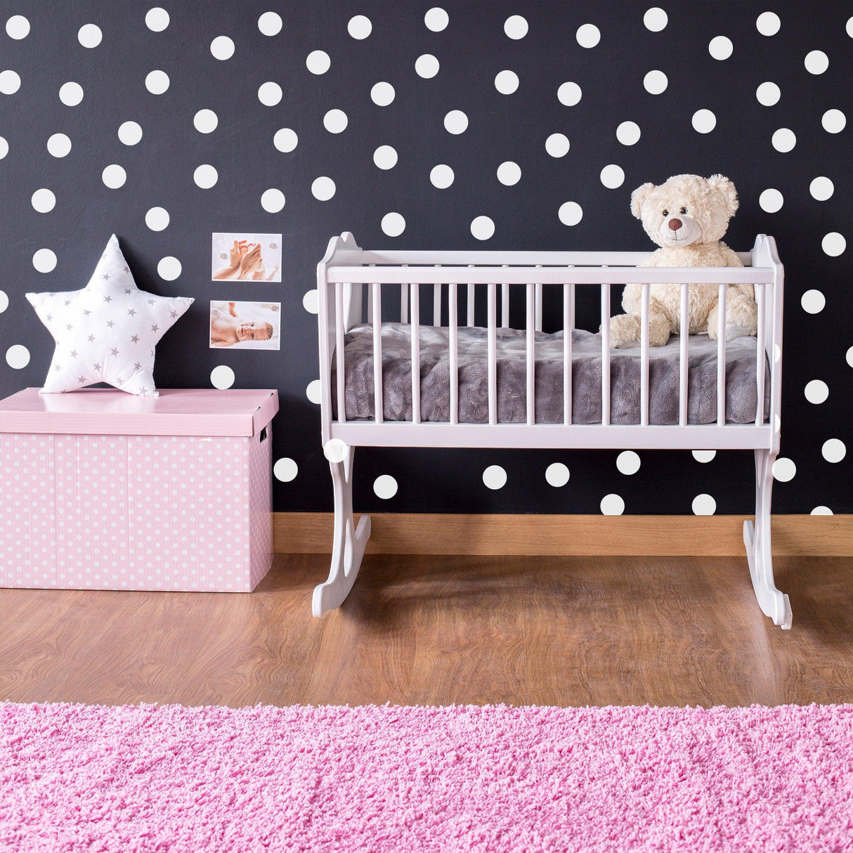 Cozy nursery featuring a white crib with teddy bear and polka dot wall decor, complemented by a pink rug and storage box.