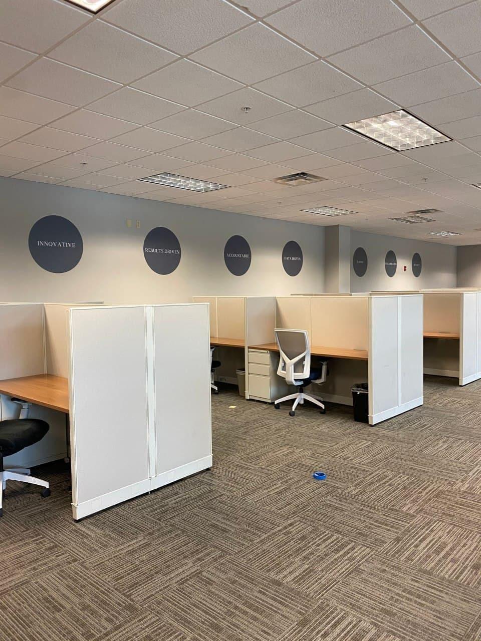 Modern office workspace with cubicles and motivational wall decals, featuring a clean and organized layout.