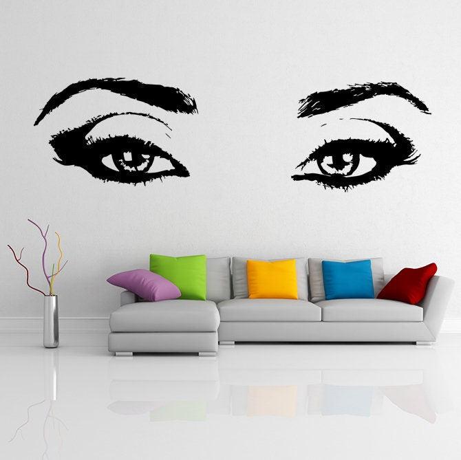 Stylish woman eyes wall sticker decor above a modern sofa with colorful cushions in a chic living room.