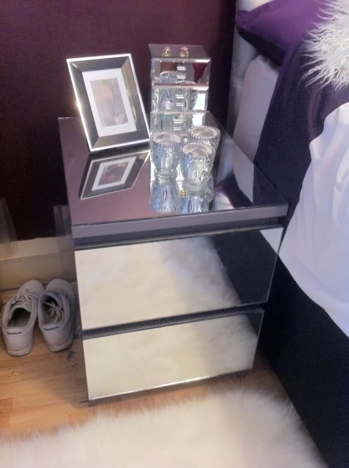 Modern mirrored nightstand with decorative items and shoes nearby, adding elegance to a bedroom decor.