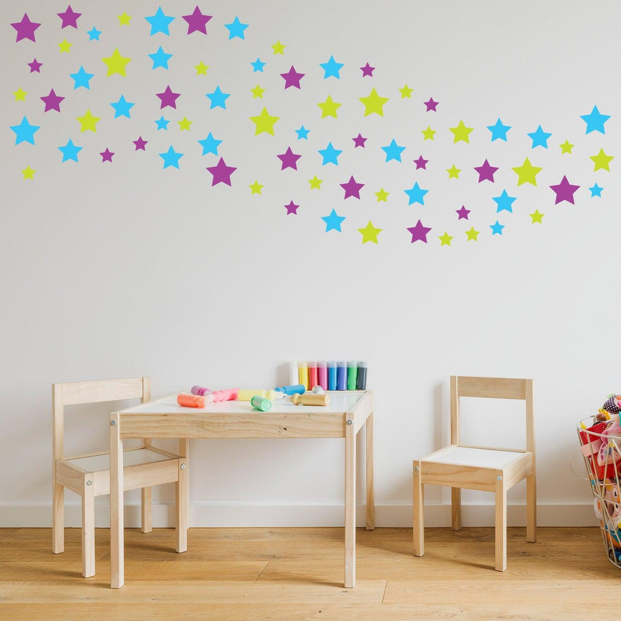 Colorful star wall decals in a nursery above a wooden table and chairs, enhancing the playful decor.