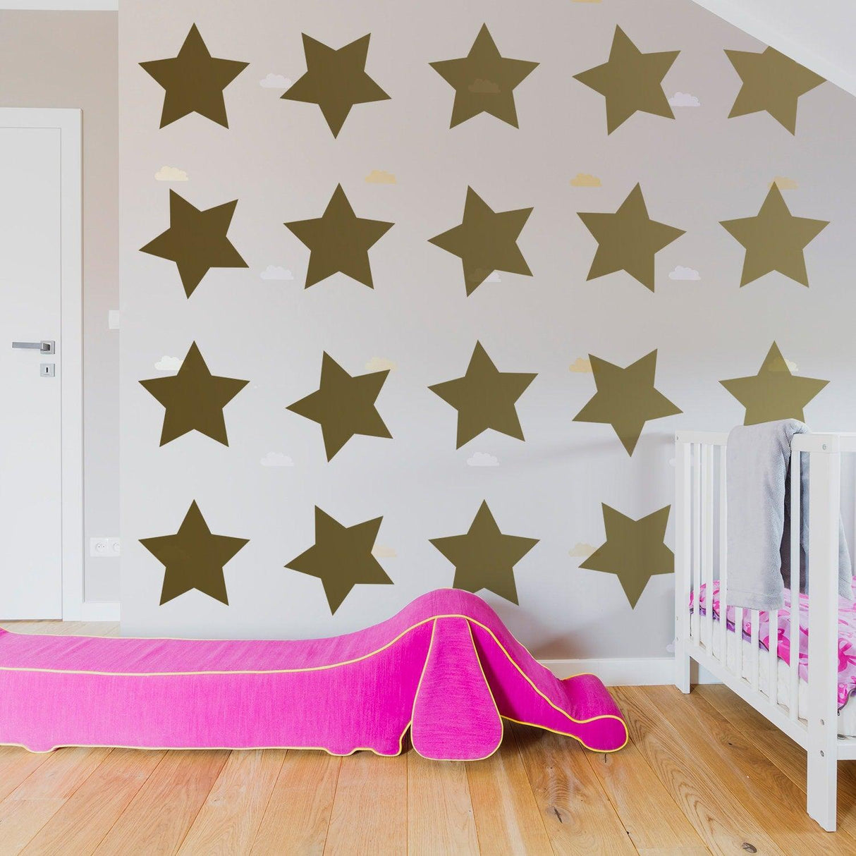 Removable star wall decals in a nursery, featuring various sizes of stars on the wall above a pink toddler bed.