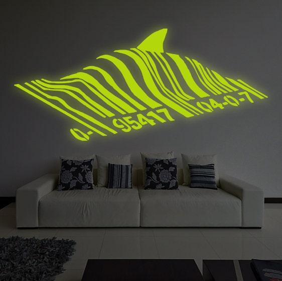 Glow-in-the-dark Banksy barcode shark vinyl sticker on a wall above a modern couch in a stylish living room.
