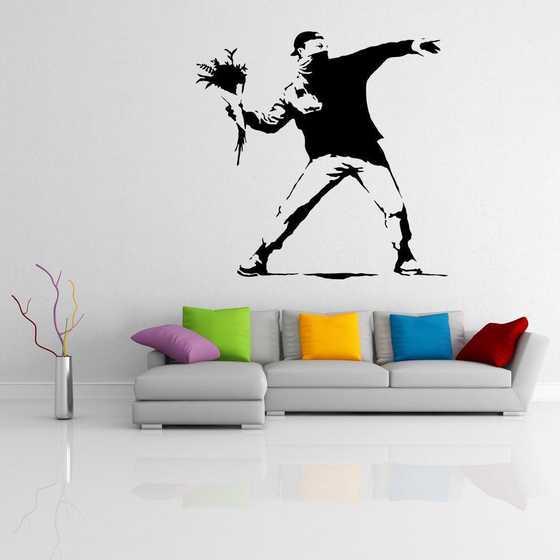 Banksy Flower Thrower wall decal in modern living room with colorful cushions on a white sofa.